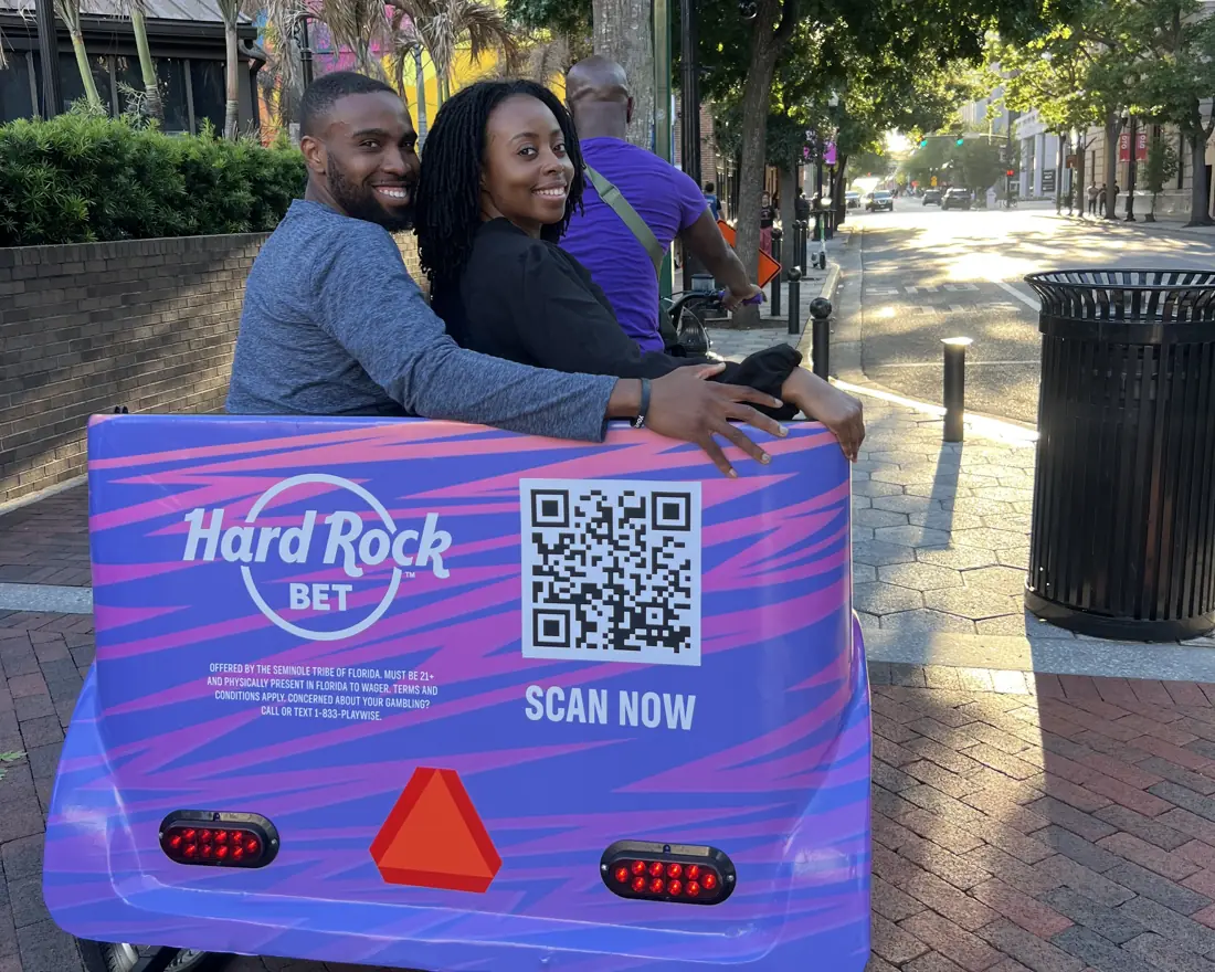 Fans riding a Hard Rock Bet pedicab with a QR code on the back panel