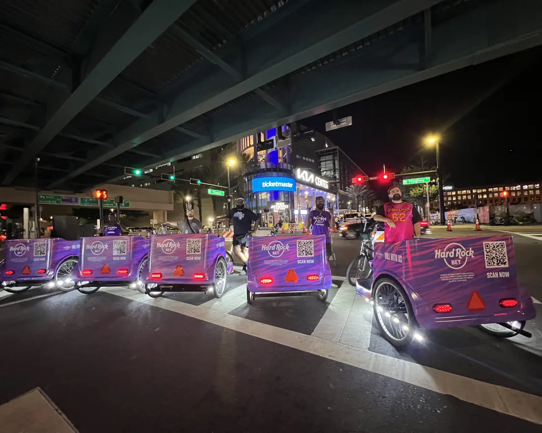 Hard Rock Bet branded pedicab fleet lined up under the overpass in downtown Orlando at night