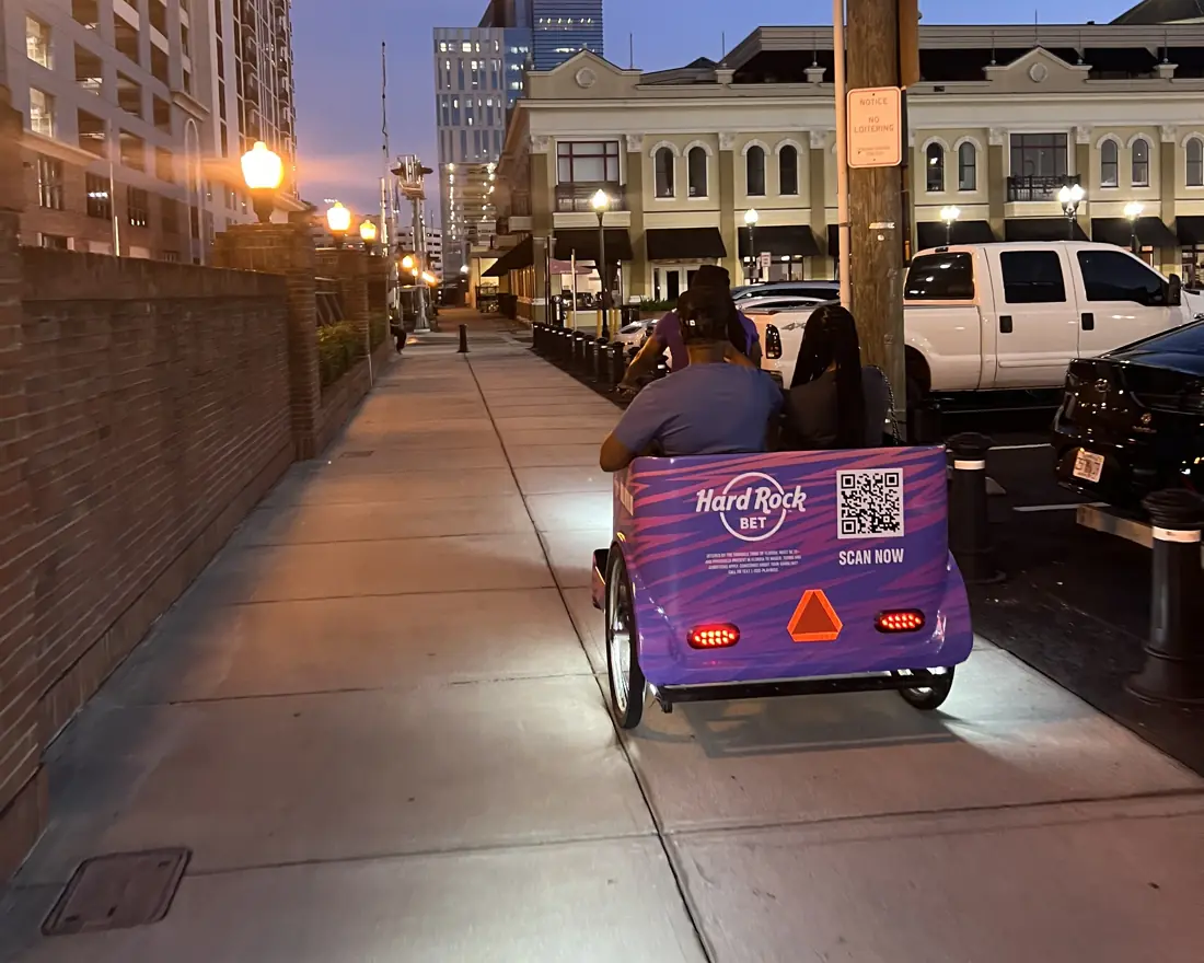 Hard Rock Bet pedicab carrying riders past downtown Orlando at dusk