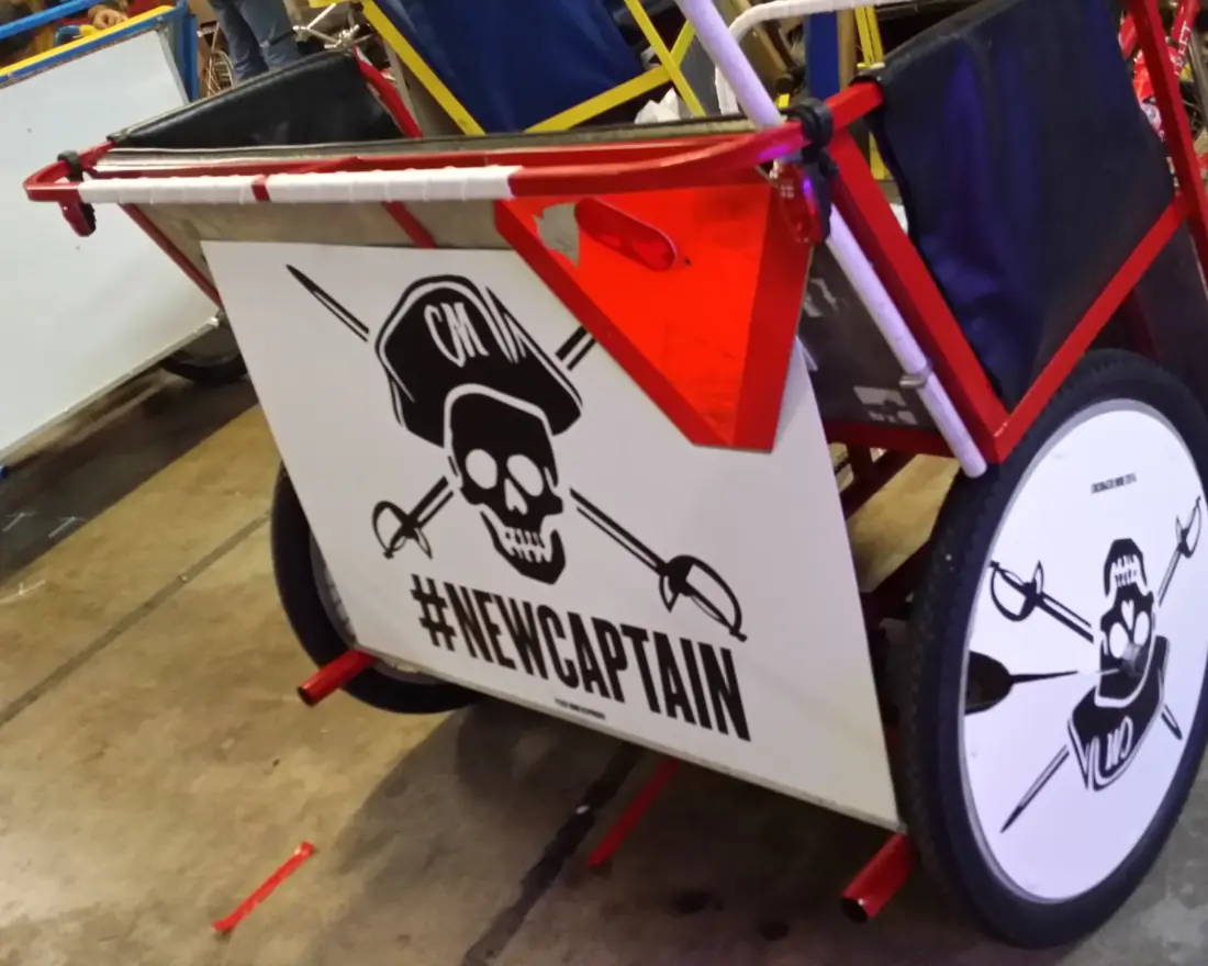 Red pedicab with #NEWCAPTAIN side panel and skull wheel cover